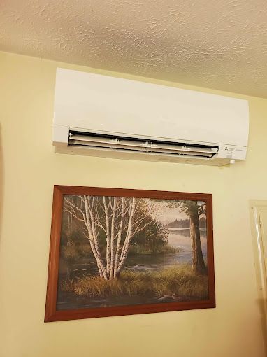 There is a picture of a tree on the wall above the air conditioner.