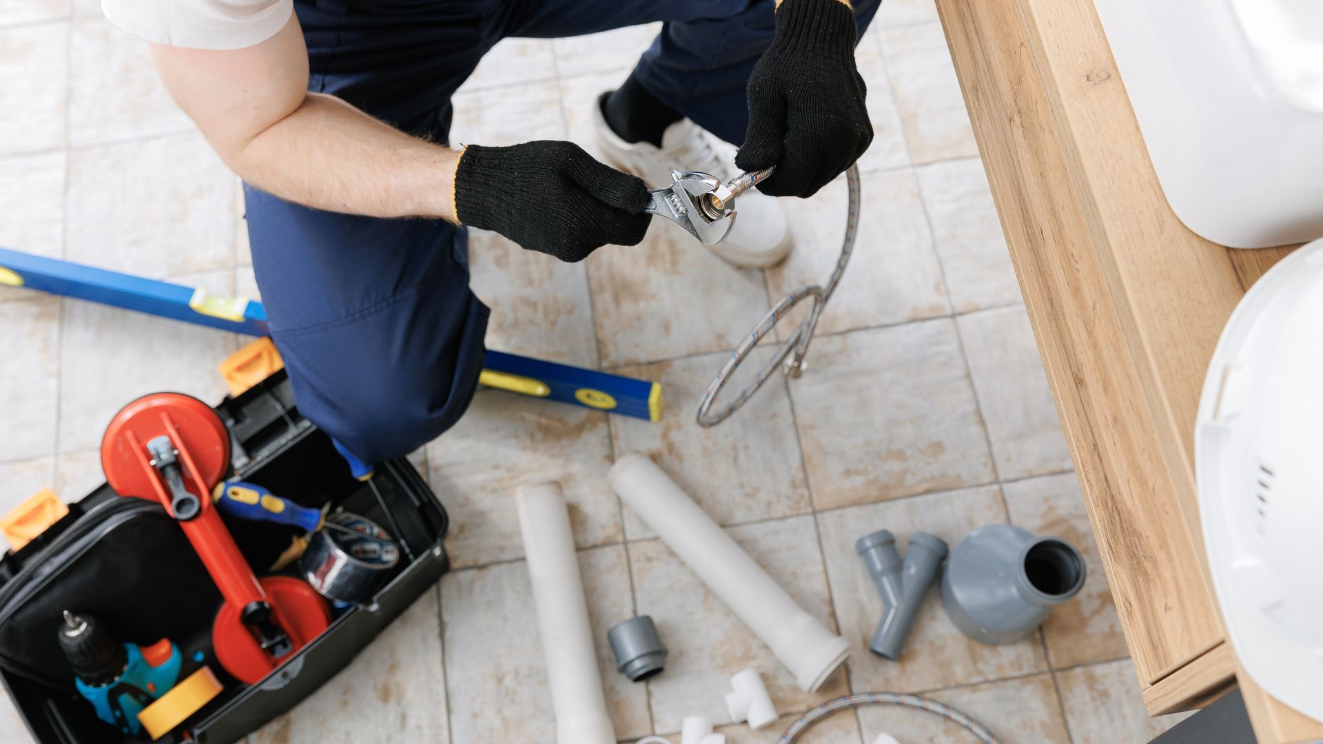 A plumber is kneeling on the floor fixing a pipe.