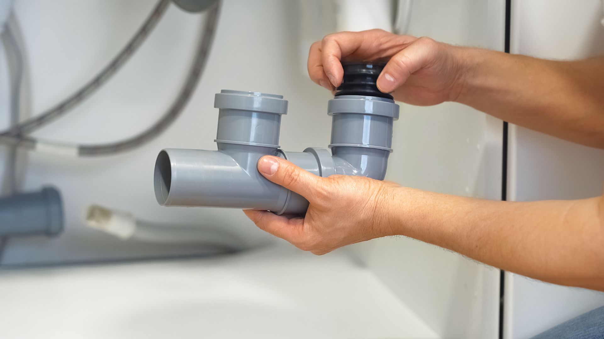 A person is fixing a pipe under a sink.