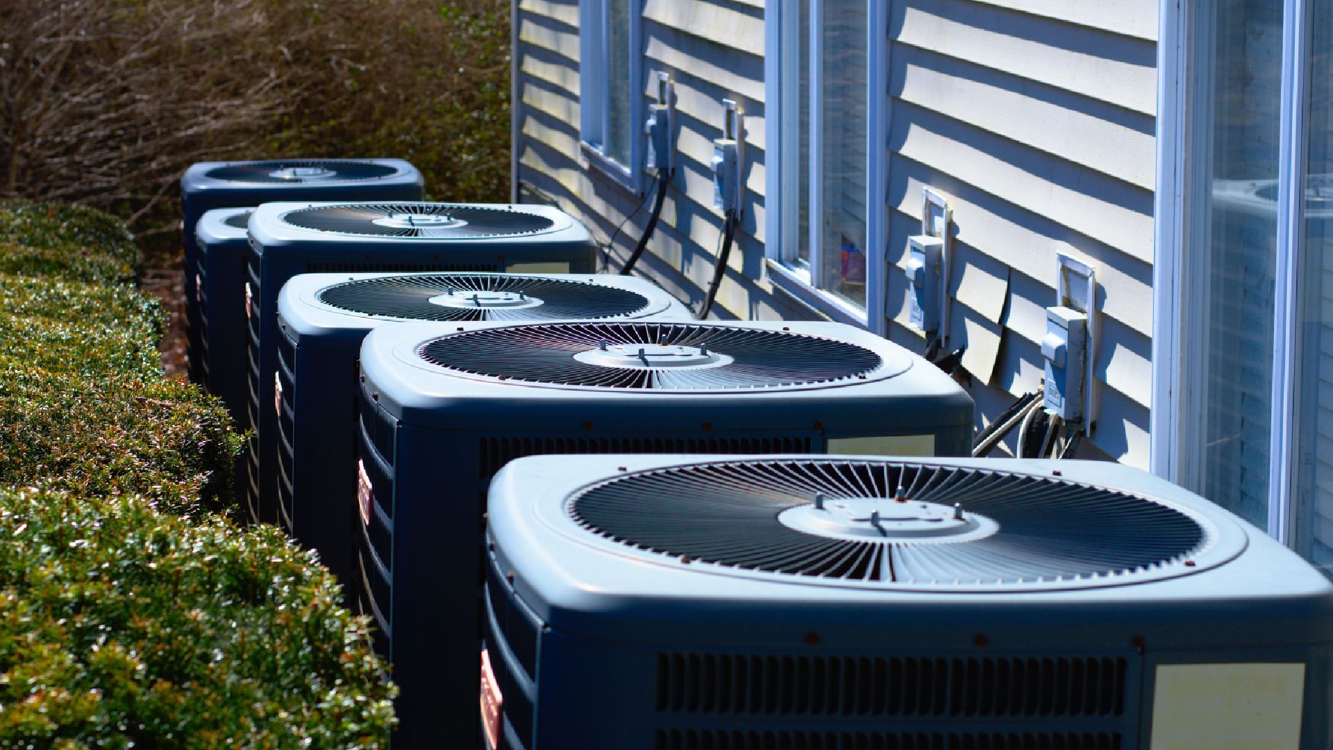 An air conditioner is sitting outside of a brick house next to a window.