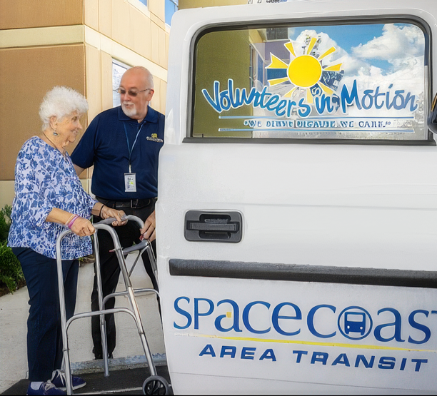 Elderly woman with walker being assisted into a Space Coast Area Transit van by a volunteer.