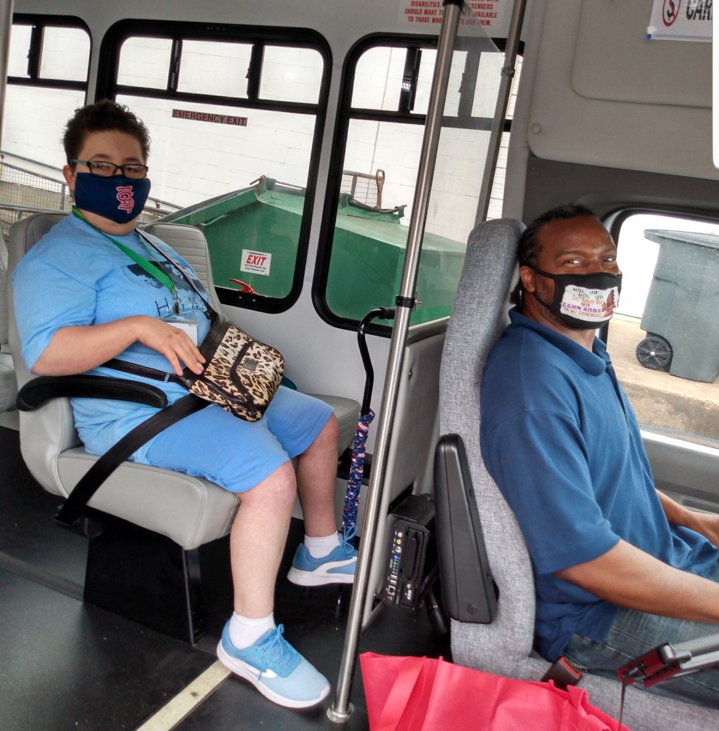 Photo of a driver and a passenger on a bus.  Both are wearing masks.