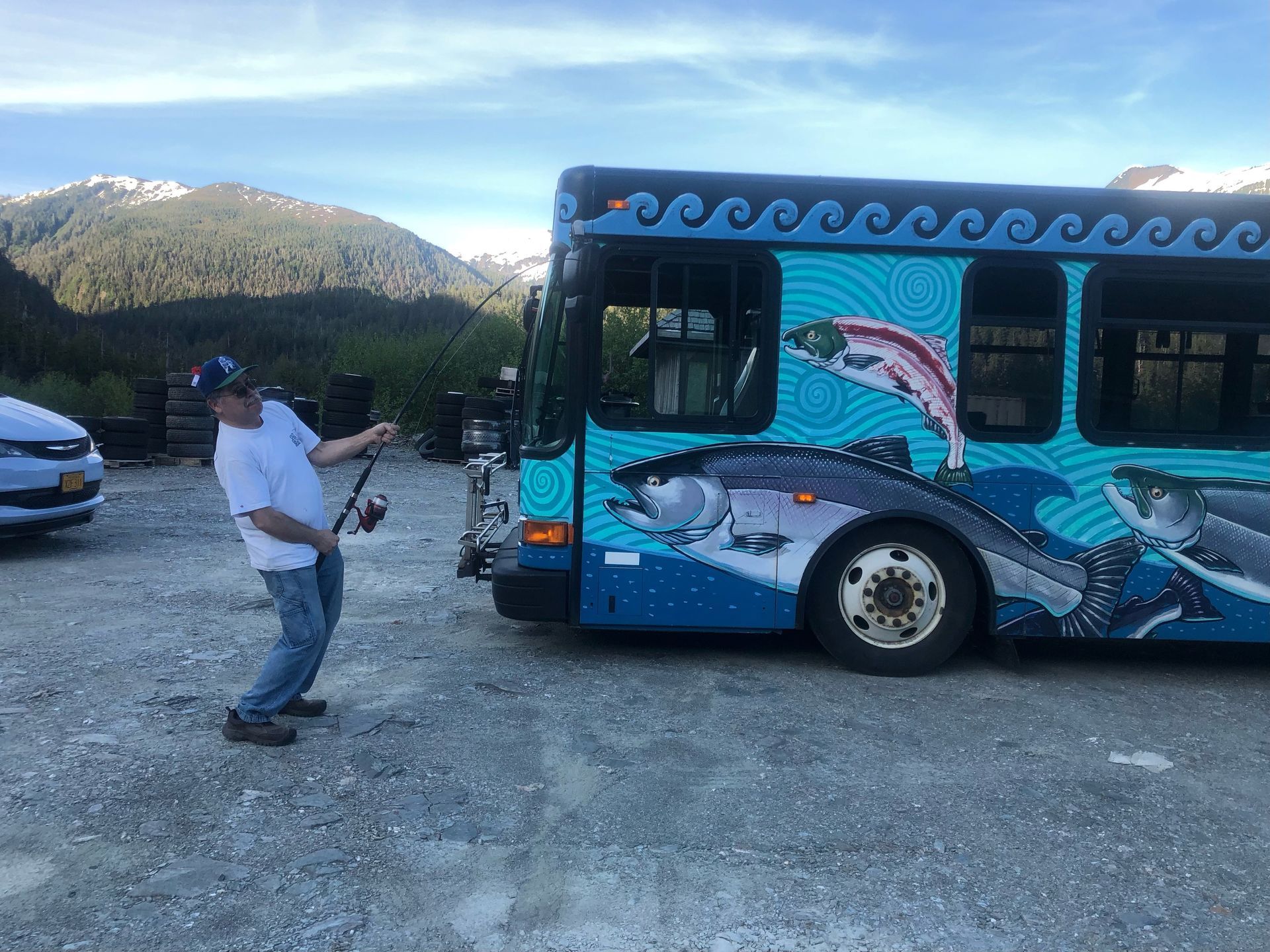 Fisherman pretending to catch a Ketchican Transit bus with a bus wrap with fishes