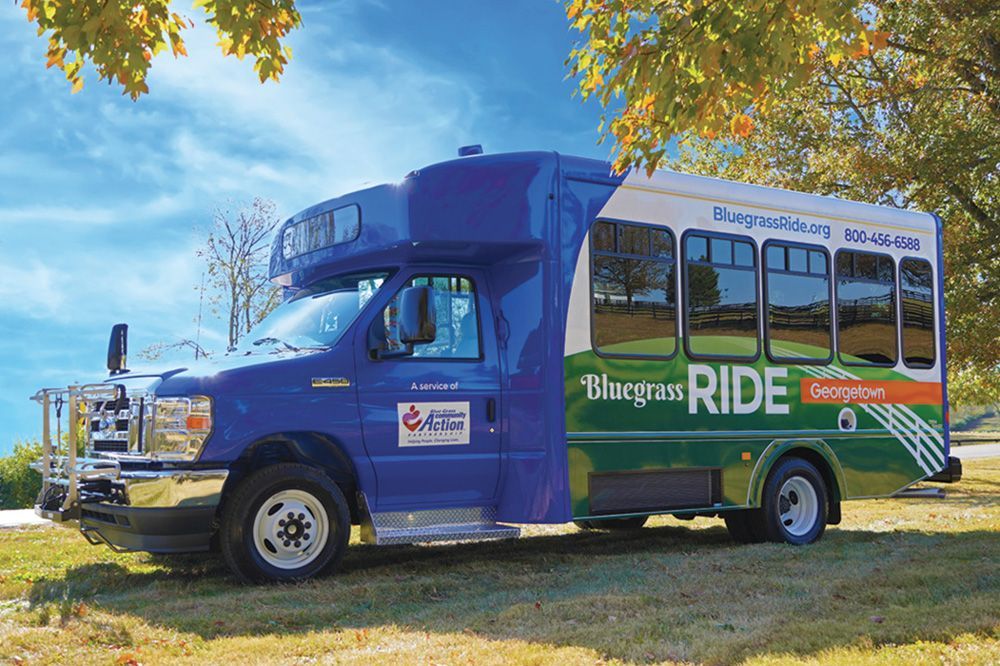 A blue and green bluegrass ride bus is parked in a grassy field.