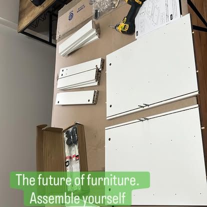 Three people in work uniforms assembling a wooden bookshelf in a bright, modern room.