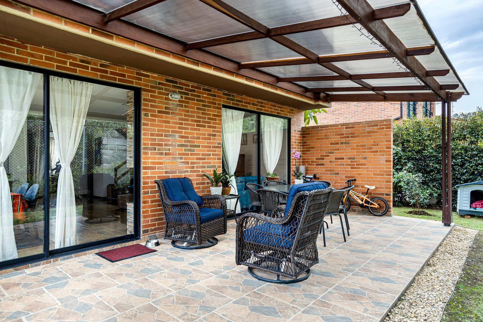 Patio with seating under a canopy, brick wall, and sliding glass doors.