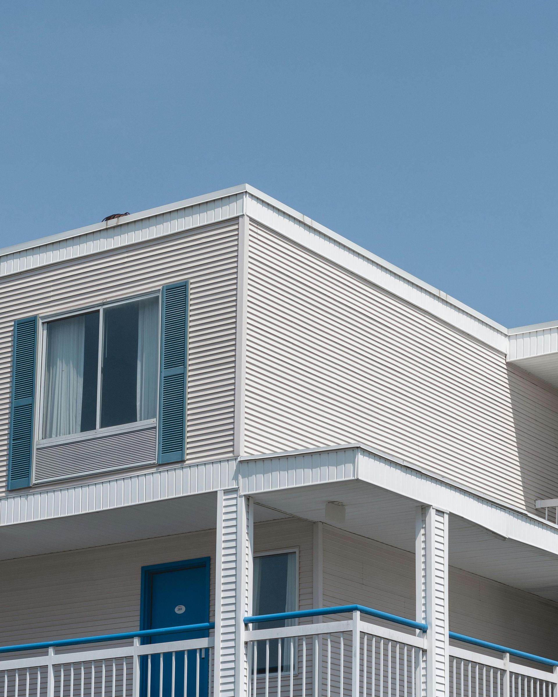 Exterior of a two-story motel with white siding, blue trim, and a blue door against a clear blue sky.