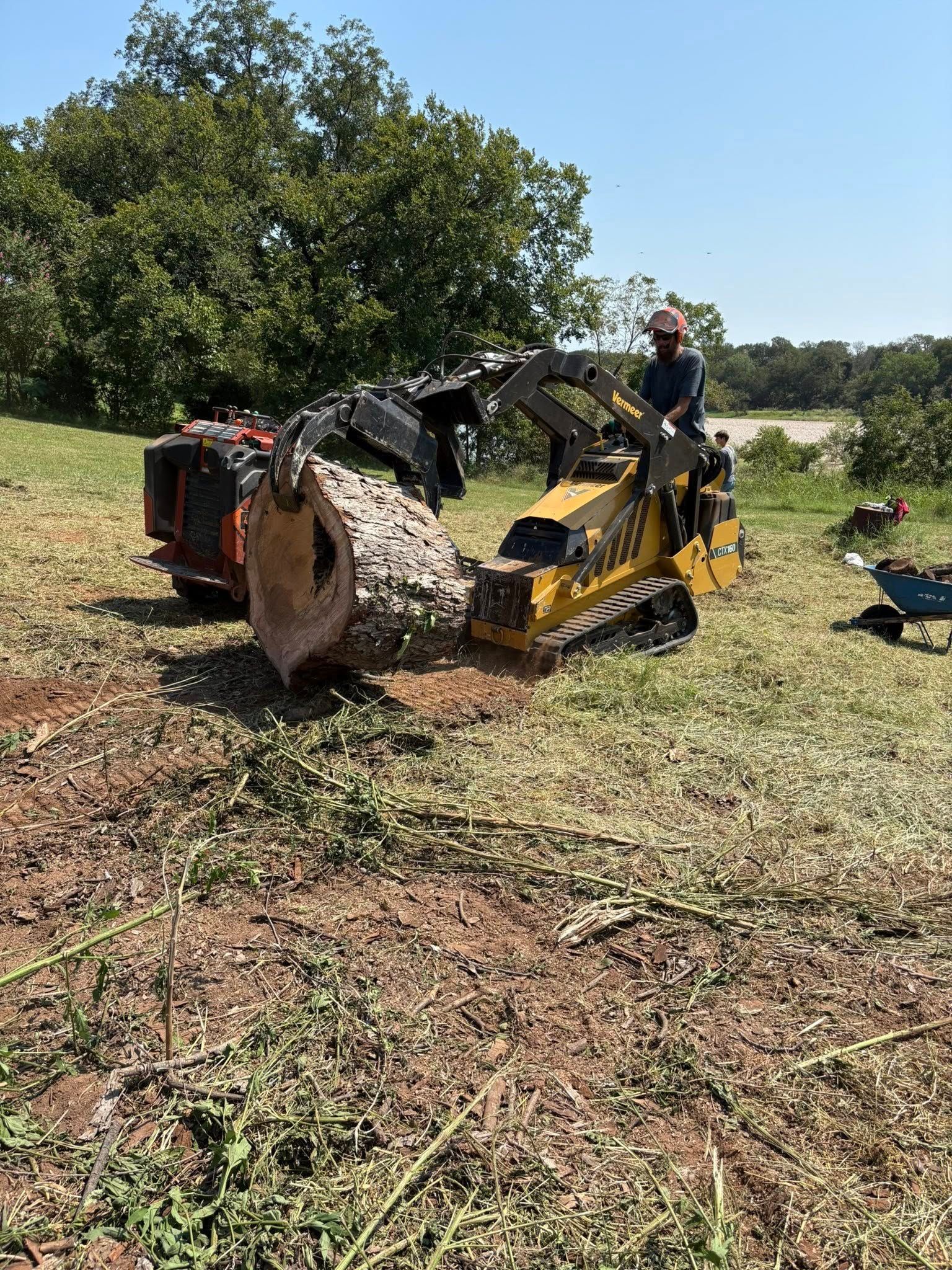 A person operating a yellow stump grinder removes a tree stump outdoors.