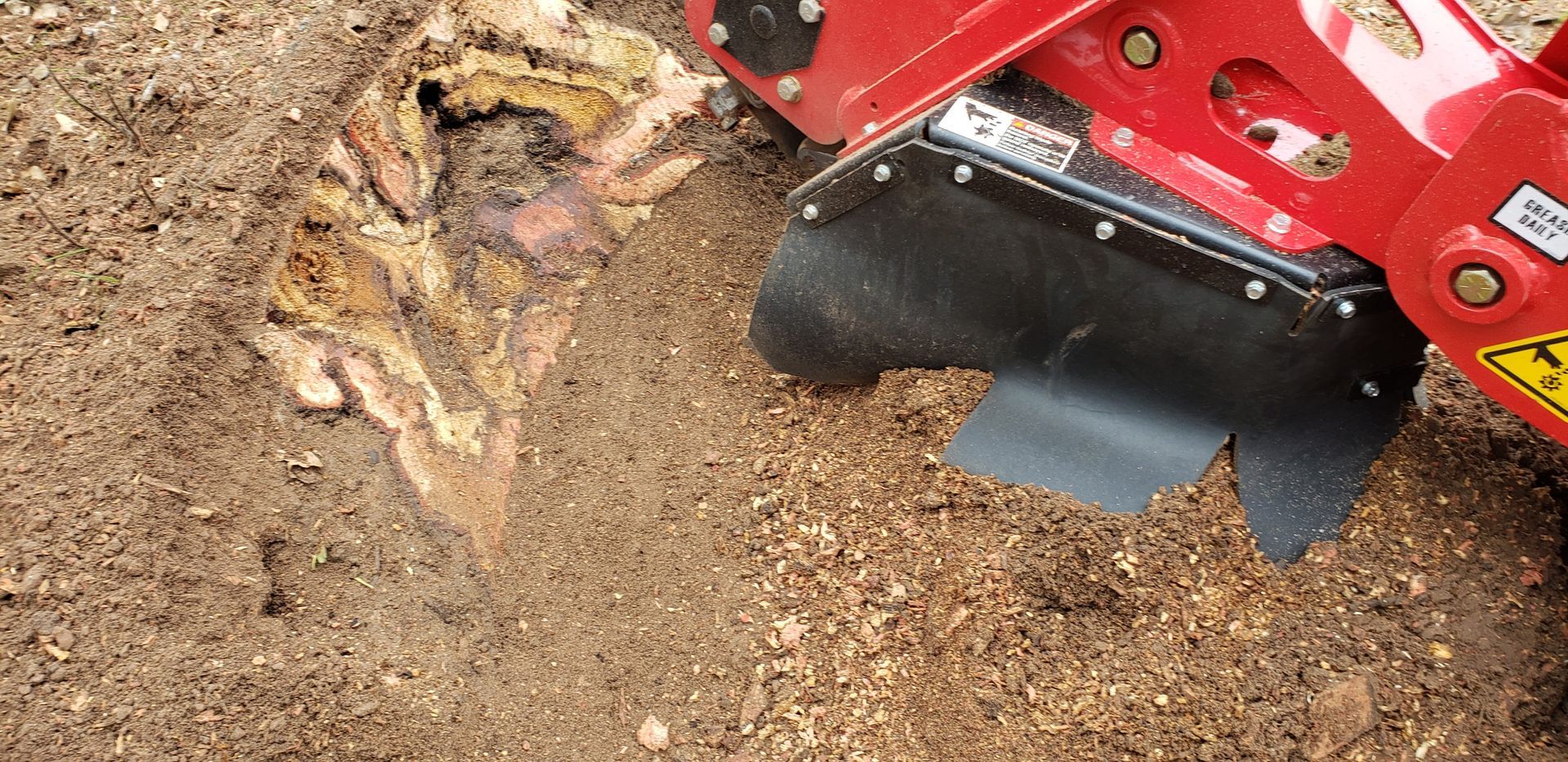 A stump grinder in action, grinding a tree stump in the dirt.