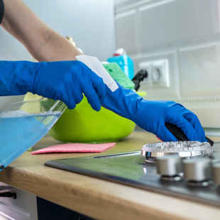 Cleaning Services Boone NC employee wearing blue gloves is cleaning a stove top with a spray bottle.