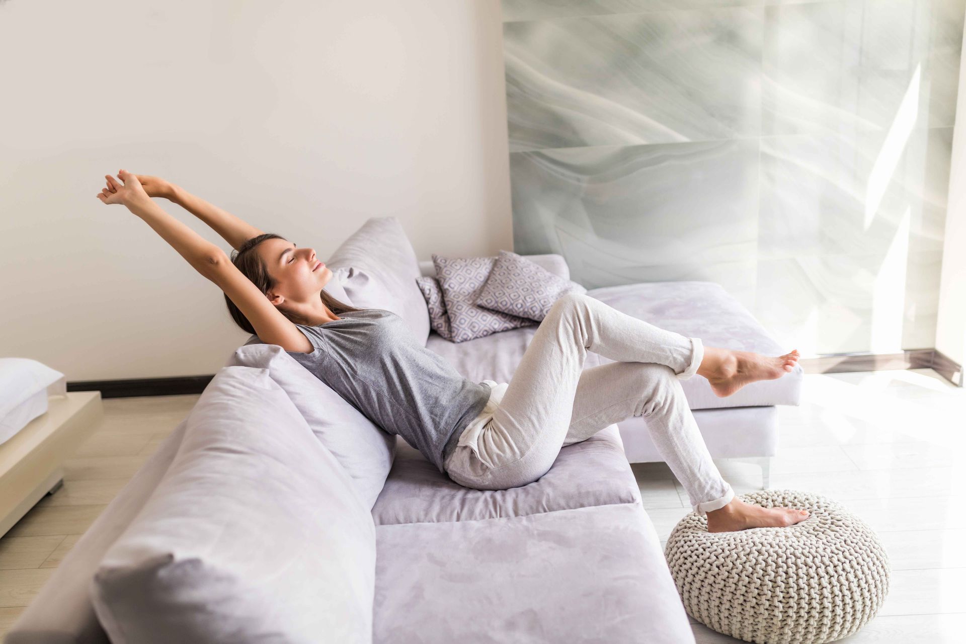 Person stretching on a gray couch in a bright living room