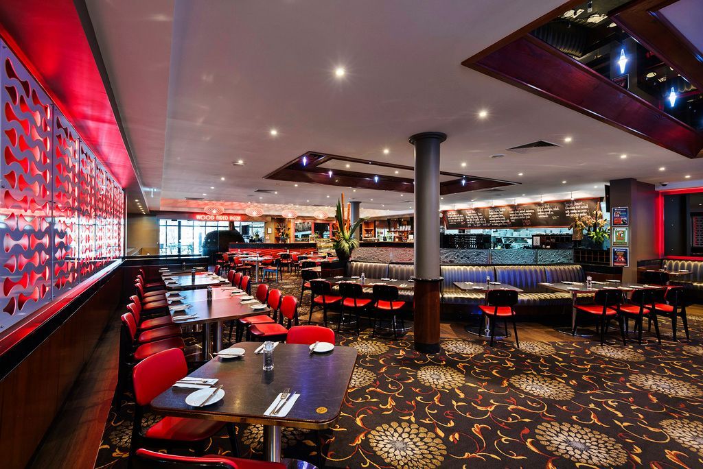 Restaurant interior with red chairs, tables, patterned carpet, and red accents.