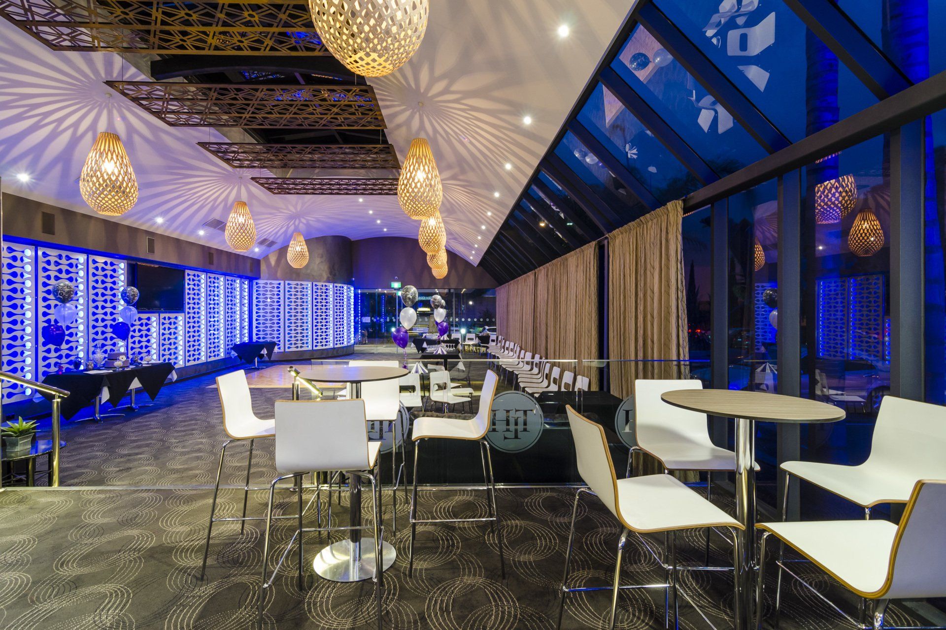 Interior of a modern event space with white chairs, tables, and decorative lighting; blue and gold accents.