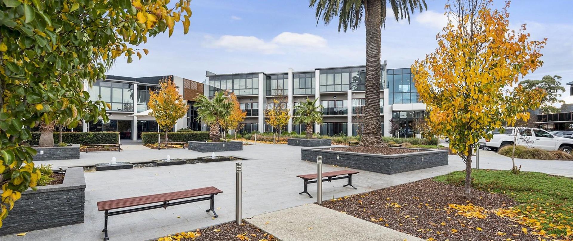 Exterior of modern commercial buildings with benches, trees, and a plaza area.
