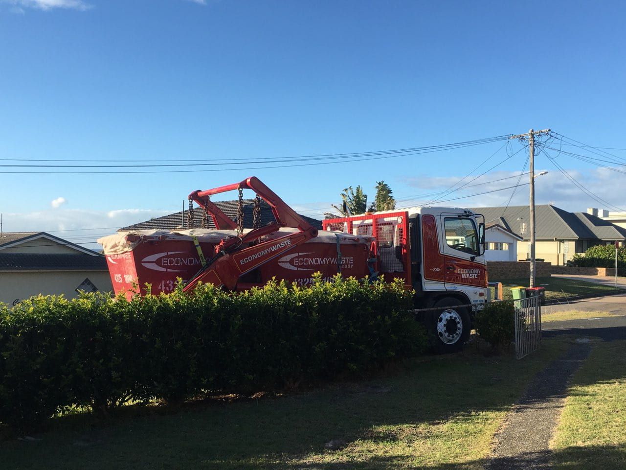 A Red And White Truck Is Parked In Front Of A Hedge — Economy Waste Group | Skip Bins Central Coast In Saratoga, NSW