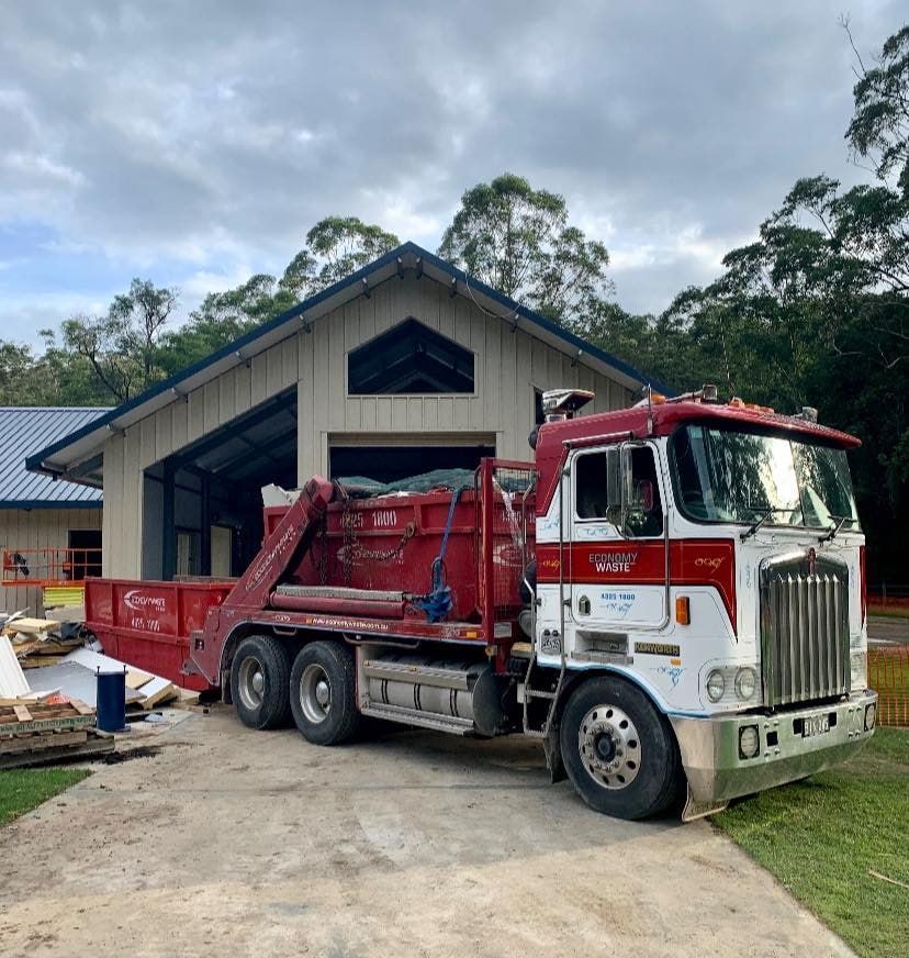 A Red And White Dump Truck Is Parked In Front Of A House — Economy Waste Group | Skip Bins Central Coast In Saratoga, NSW
