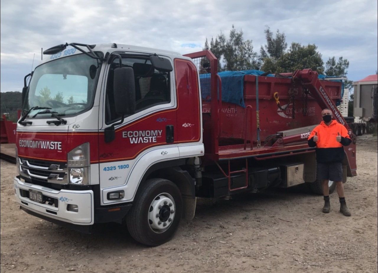 A Man Is Standing In Front Of A Red Truck — Economy Waste Group | Skip Bins Central Coast In Chittaway Bay, NSW