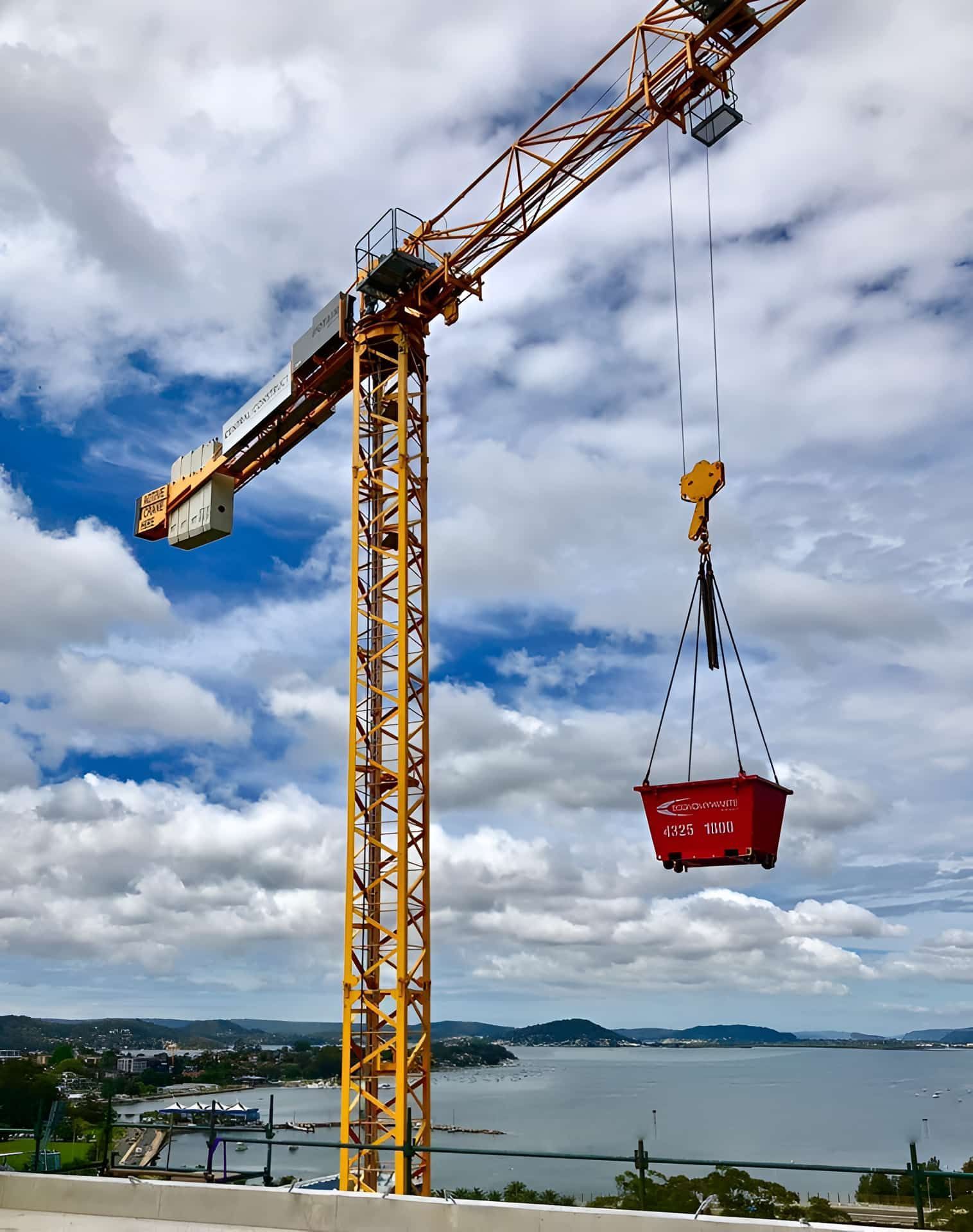 A Construction Crane Is Lifting A Red Bin Over A Body Of Water — Economy Waste Group | Skip Bins Central Coast In West Gosford, NSW