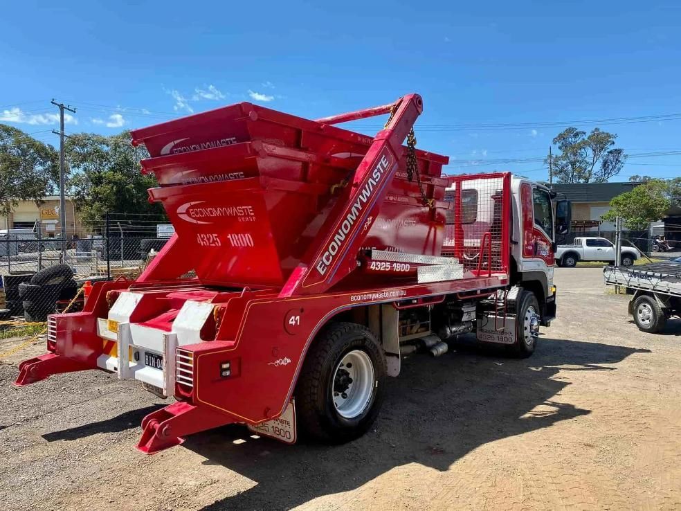 A Red Dump Truck Is Parked In A Dirt Lot — Economy Waste Group | Skip Bins Central Coast In Ourimbah, NSW