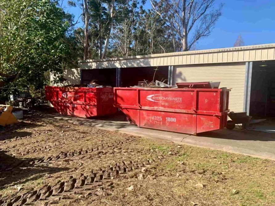 Two Red Dumpsters Are Parked In Front Of A Garage — Economy Waste Group | Skip Bins Central Coast In Lake Haven, NSW