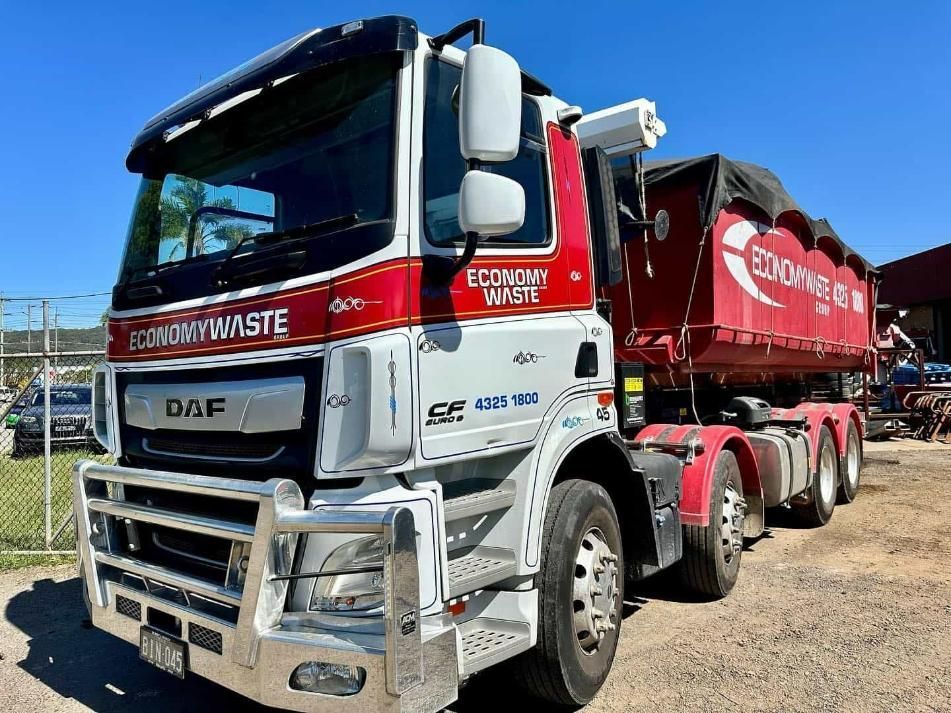 A Red And White Dump Truck Is Parked In A Dirt Lot — Economy Waste Group | Skip Bins Central Coast In Warnervale, NSW