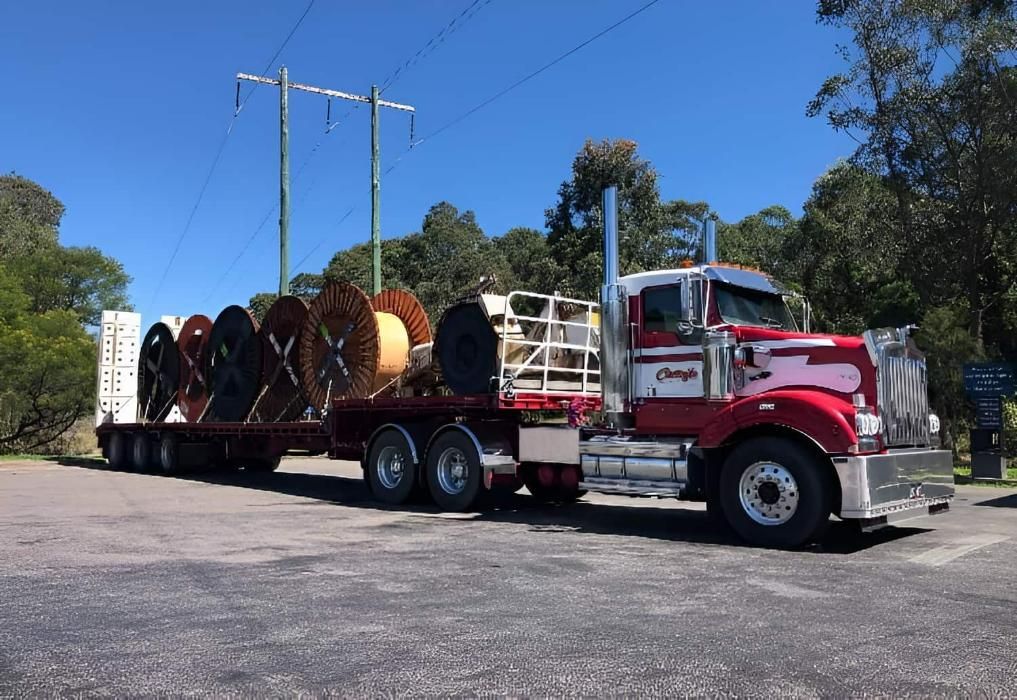 A Red Semi Truck Is Carrying Spools Of Wire On A Flatbed Trailer  — Economy Waste Group | Skip Bins Central Coast In Lake Munmorah, NSW