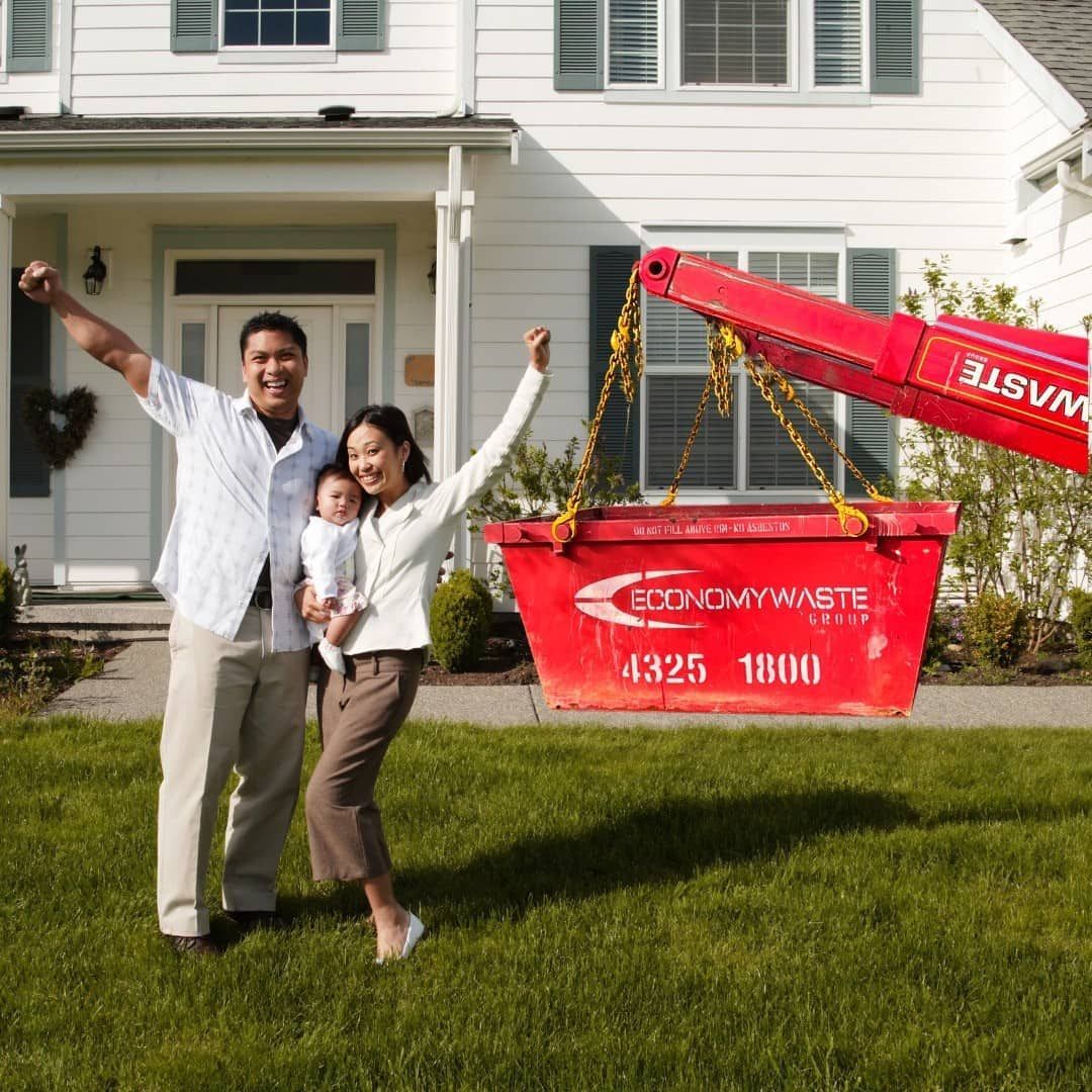 A Man And Woman Standing In Front Of A Red Dumpster That Says Economy Waste — Economy Waste Group | Skip Bins Central Coast In Woy Woy, NSW