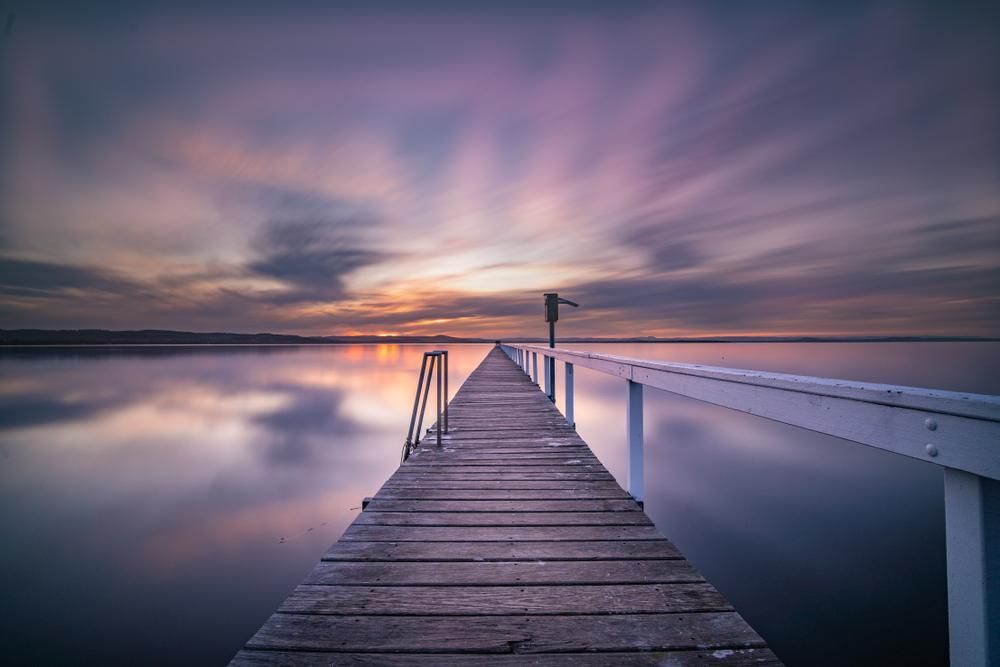 A Long Wooden Pier Leading Into A Body Of Water At Sunset — Economy Waste Group | Skip Bins Central Coast In Long Jetty, NSW