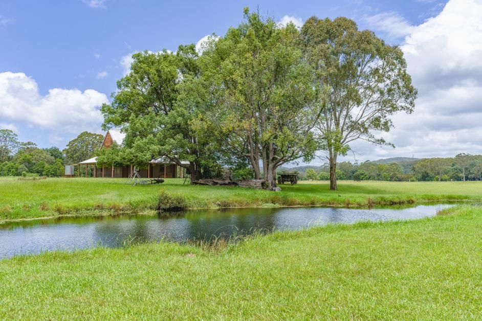 A House Is Sitting In The Middle Of A Grassy Field Next To A River — Economy Waste Group | Skip Bins Central Coast In Ourimbah, NSW