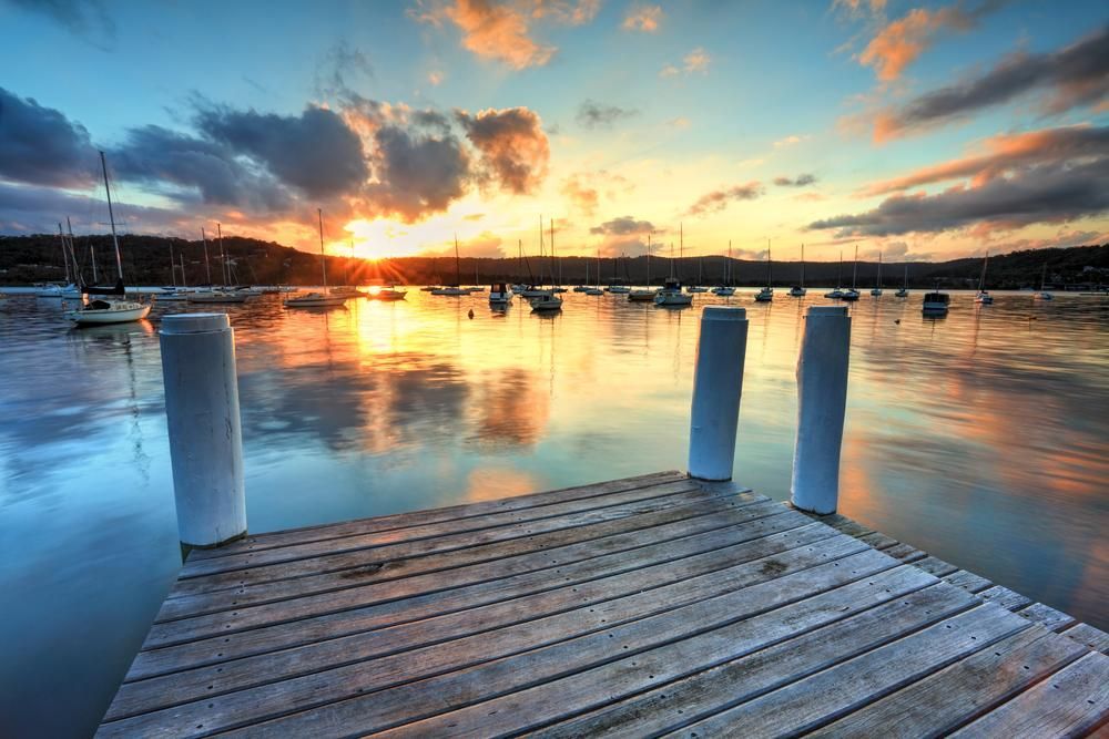 A Wooden Dock Overlooking A Body Of Water At Sunset — Economy Waste Group | Skip Bins Central Coast In Point Frederick, NSW