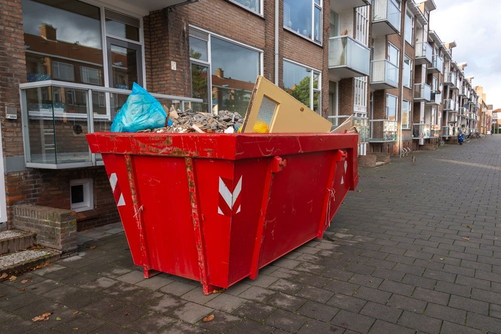 A Red Dumpster Is Sitting On The Sidewalk In Front Of A Building  — Economy Waste Group | Skip Bins Central Coast In Lake Munmorah, NSW