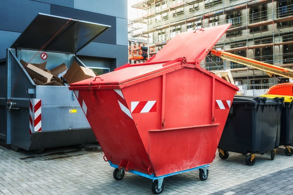 A Red Dumpster Is Parked In Front Of A Building — Economy Waste Group | Skip Bins Central Coast In Bateau Bay, NSW