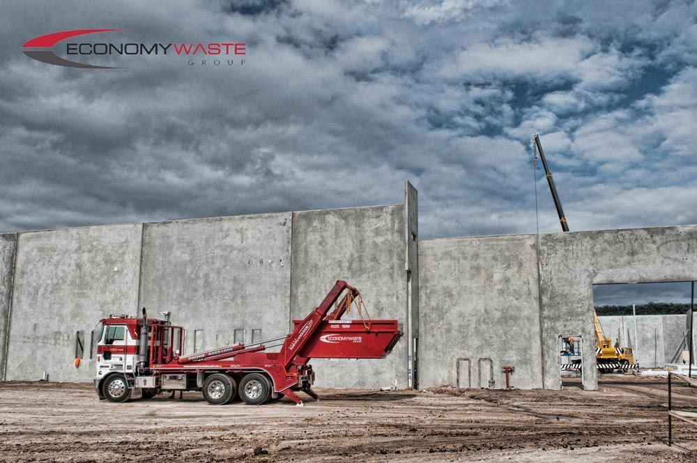 A Red Dump Truck Is Parked In Front Of A Building Under Construction — Economy Waste Group | Skip Bins Central Coast In Gosford, NSW