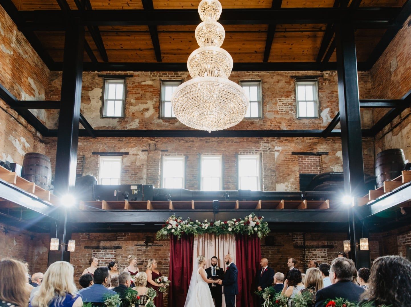 A bride and groom are getting married in a large room with a chandelier hanging from the ceiling.