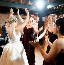 A bride and her bridesmaids are dancing together at a wedding reception.