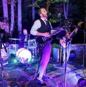 A man is singing into a microphone while playing a guitar in a band.