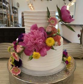 A white cake decorated with pink and yellow flowers on a silver plate.