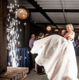 A man is holding a bride in his arms in front of a fireworks display.