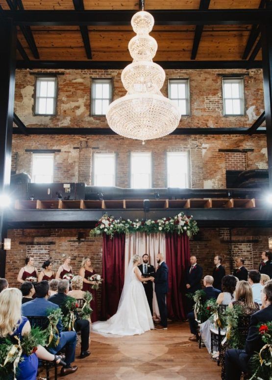 A bride and groom are getting married in a large room with a chandelier hanging from the ceiling.