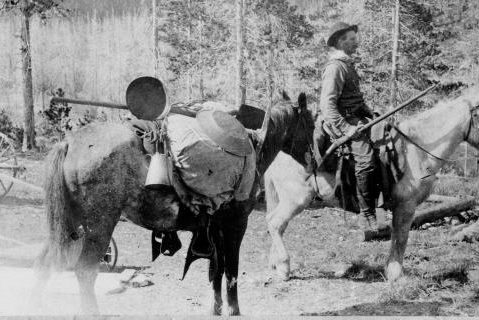 A black and white photo of two men riding horses.