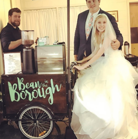 A bride and groom are standing in front of a bean in the borough cart