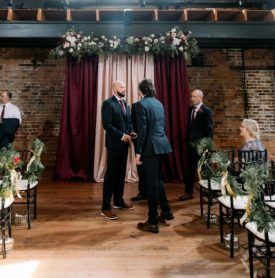 A group of men are standing in front of a row of chairs at a wedding ceremony.