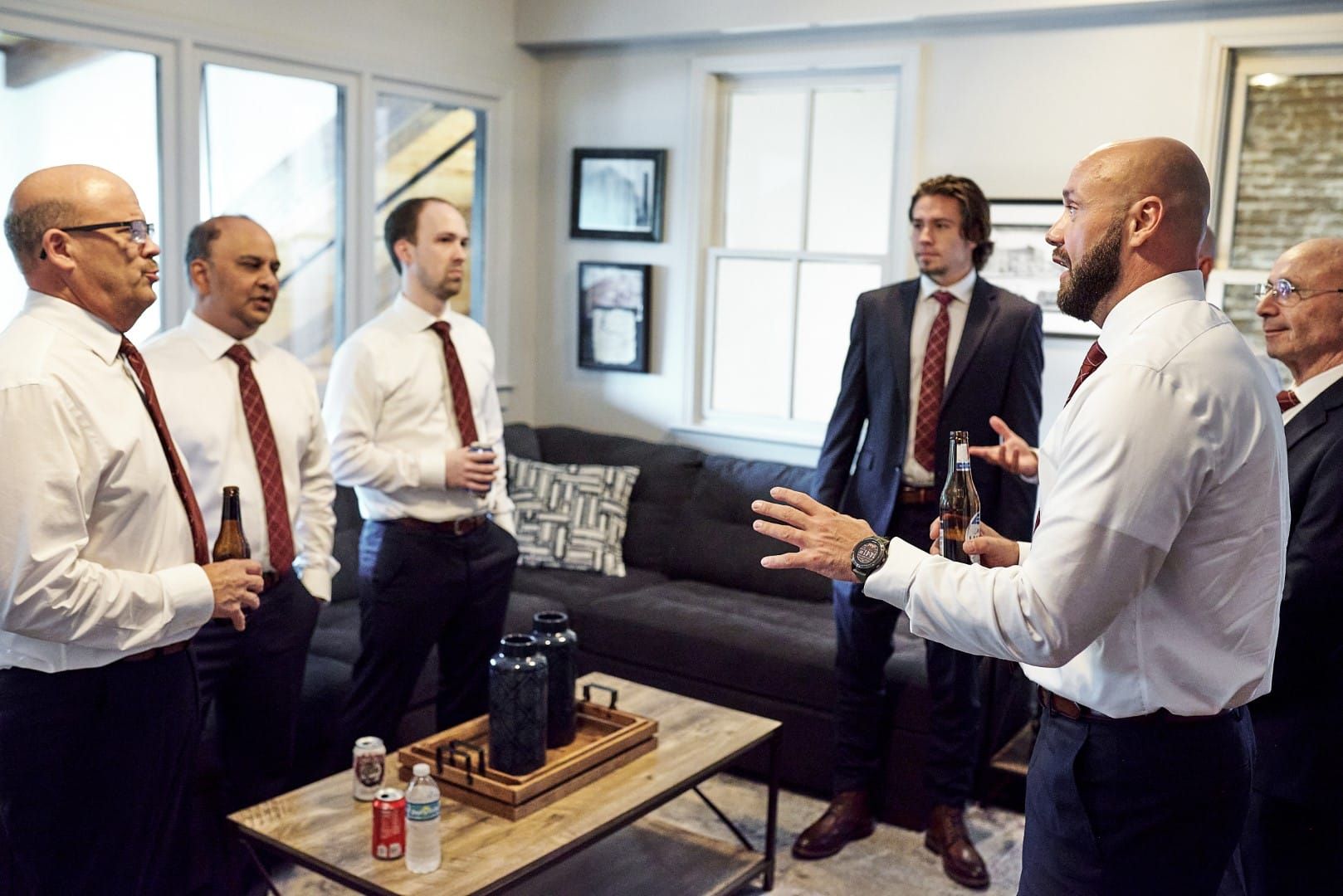 A group of men are standing around a coffee table in a living room.