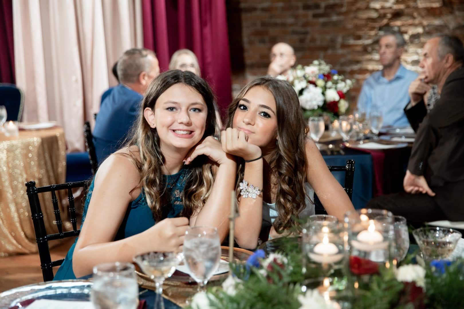 Two young women are sitting at a table at a wedding reception.