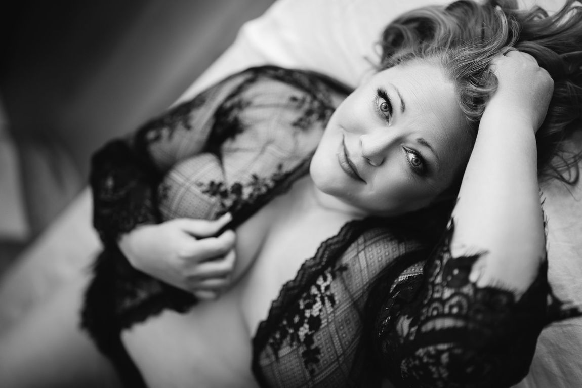 A woman dressed in delicate lingerie lies on a bed, showcasing a blend of elegance and sensuality in a tranquil atmosphere.