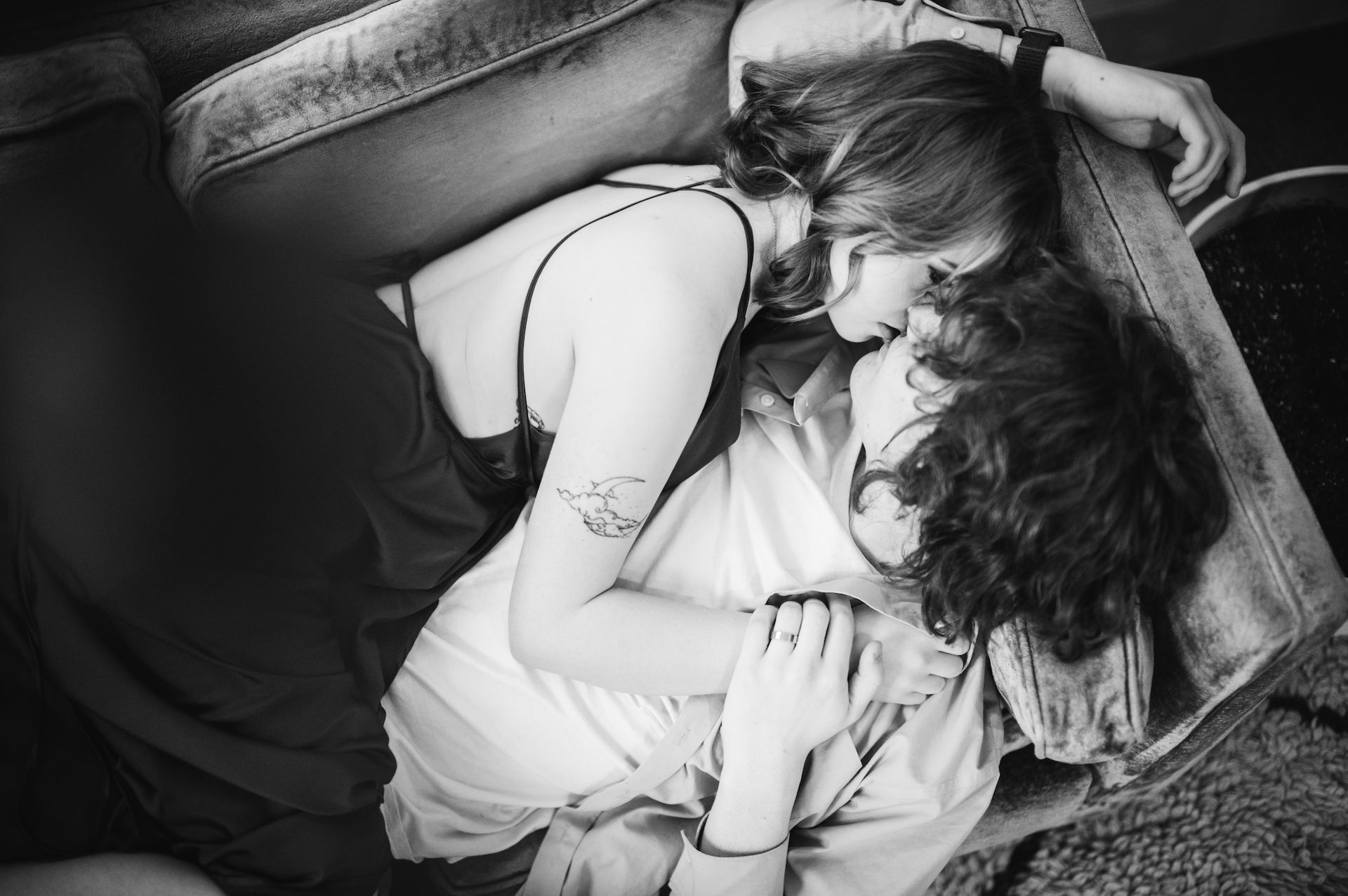a couple lying on a couch , a girl with a tattoo in her arms and a curly man wearing a ring