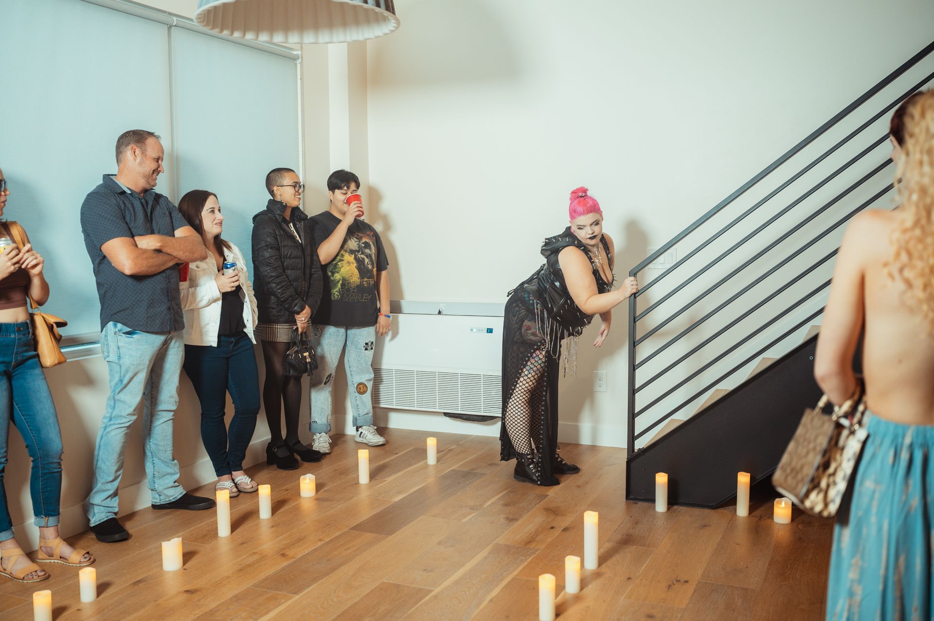 Guests at the Silk + Salt Fashion Show congregate near a staircase illuminated by candles, adding a touch of sophistication.