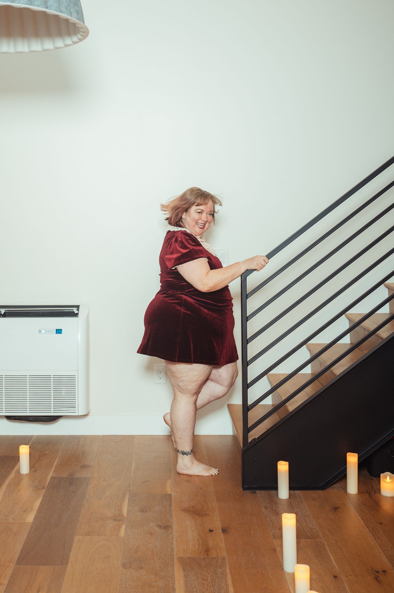 A woman in a red dress stands gracefully on a stairway, exuding elegance and poise in her surroundings.