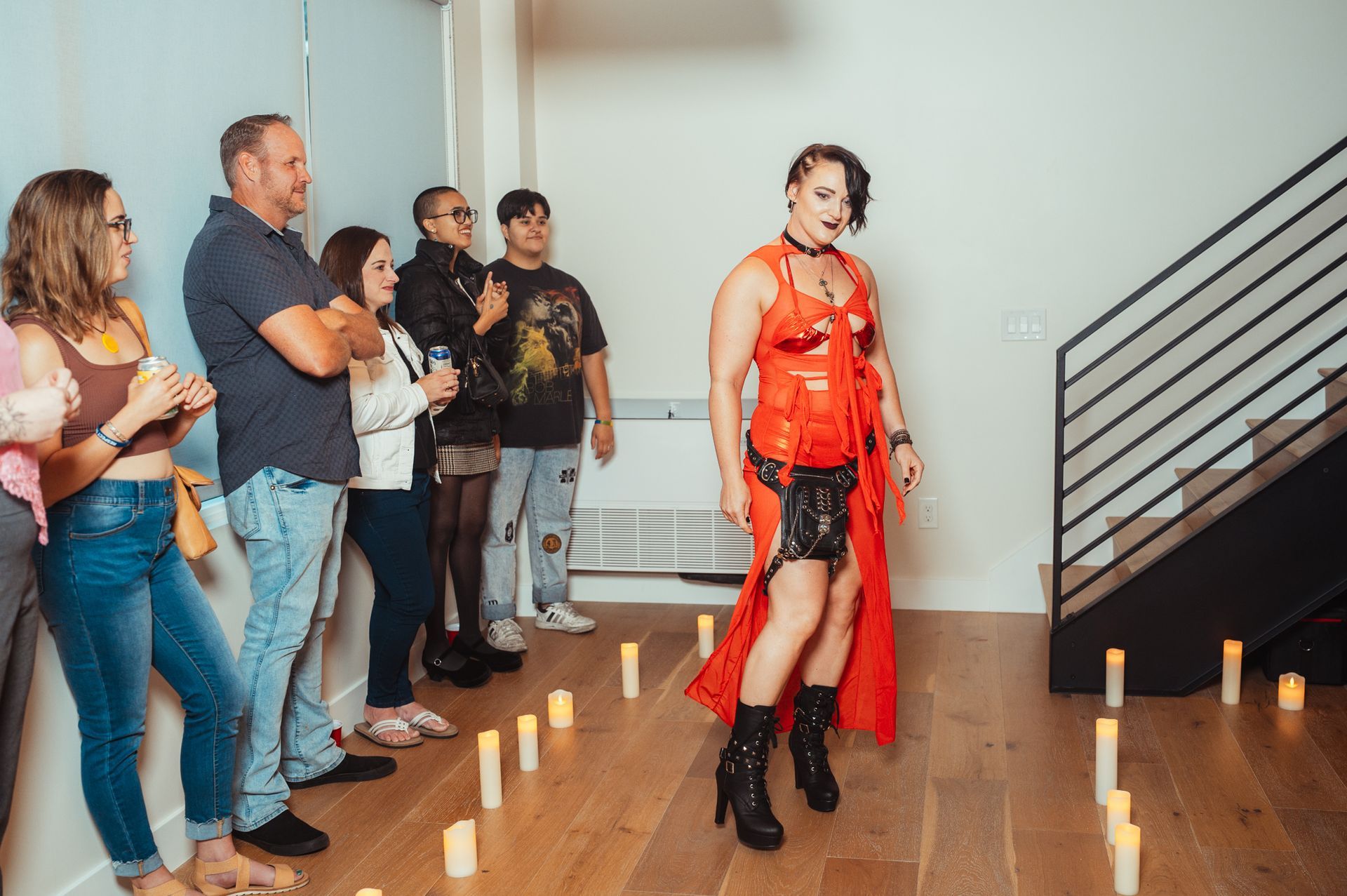 A woman in a red dress and black boots stands before a group, capturing attention with her bold fashion choice.