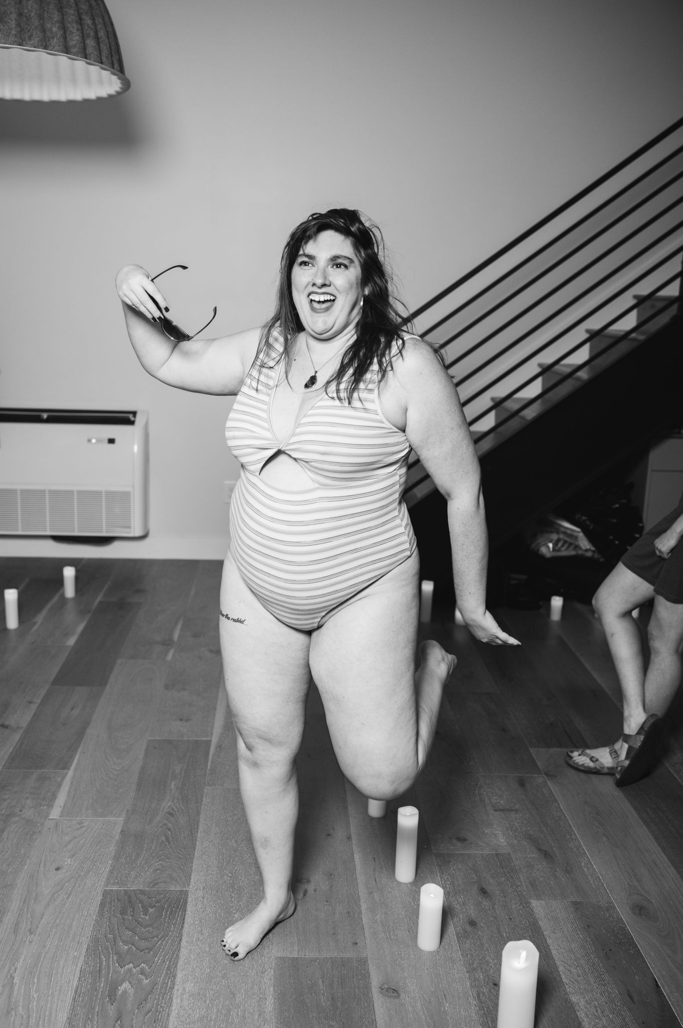 A woman in a bikini joyfully dances in the center of a spacious room, showcasing her vibrant energy and confidence.